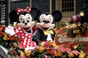 Photo of Mickey and Minnie Mouse riding in a parade float alongside a sign that says, "Disney Parks."