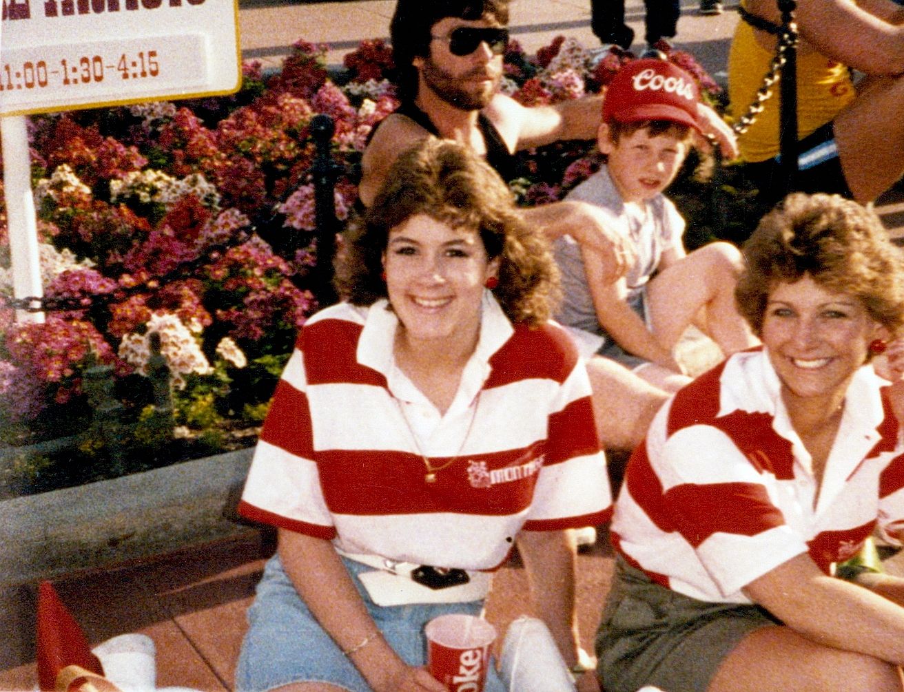 Two girls in red striped shirts sitting on a bench at a Disneyland parade. 
