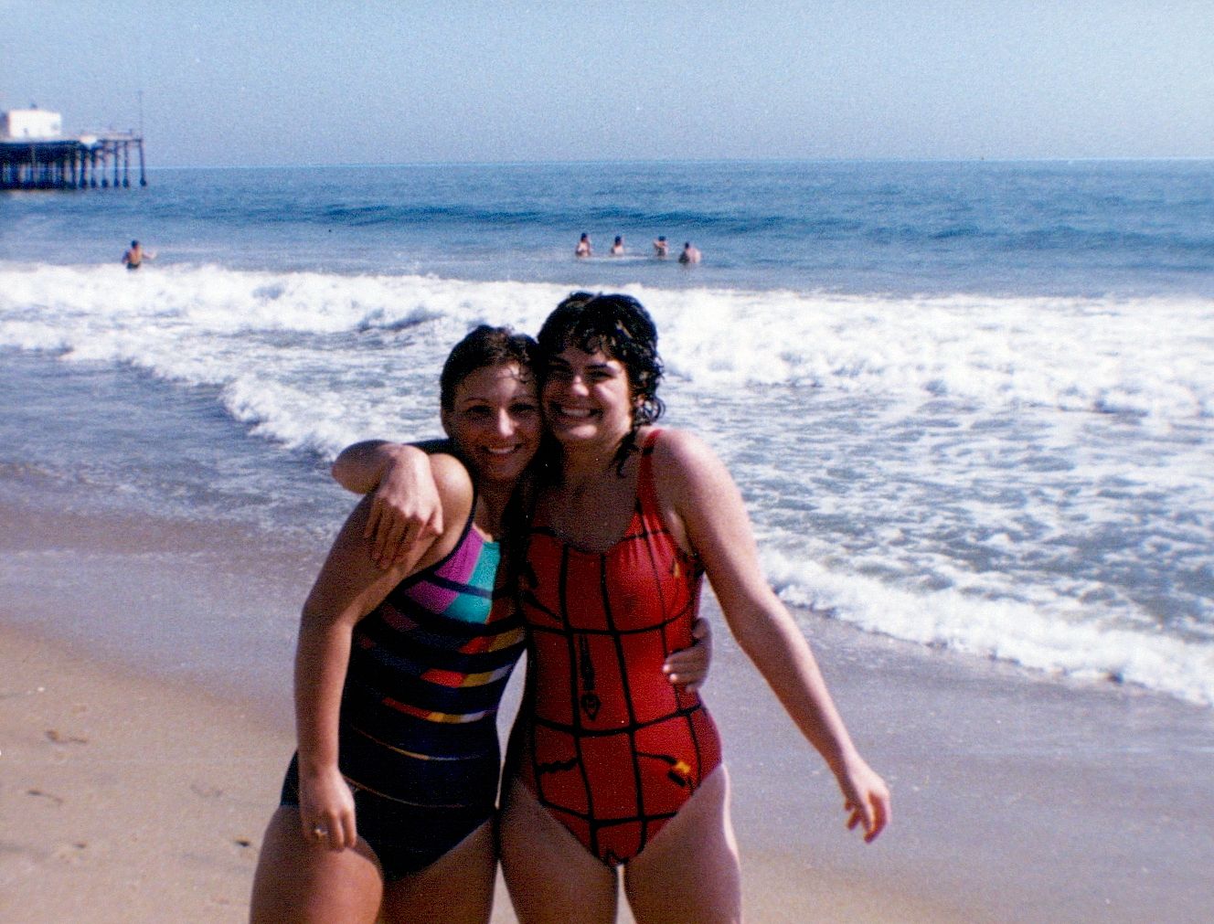 Photo of two girls in bathing suits standing on the beach.