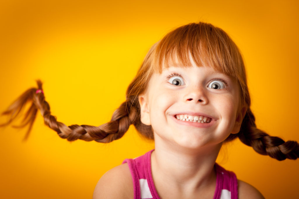 Image of a smiling red-haired girl with upward braids and a look of excitem...